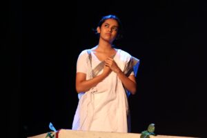 A female theatre actor in a white outfit performing a solo scene on stage